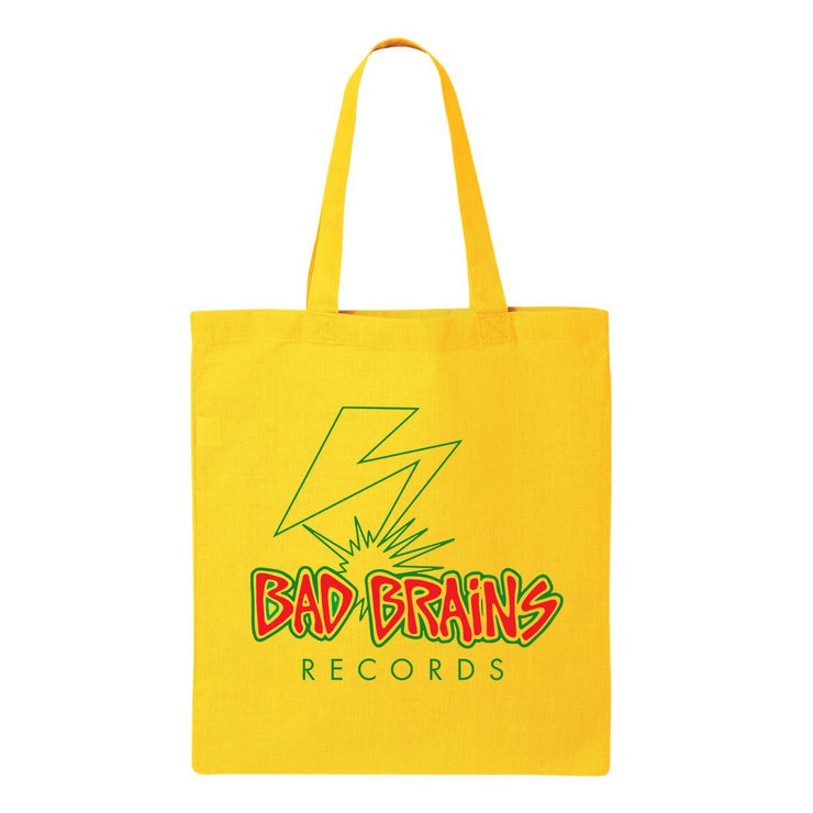 Photo of a yellow tote bag against a white background. The bag features the bad brains logo- it says Bad Brains in red lettering outlined in yellow and then outlined again in green. Below that in green reads "records". Above the text is a lightning bolt that is outlined in green, with no fill color.