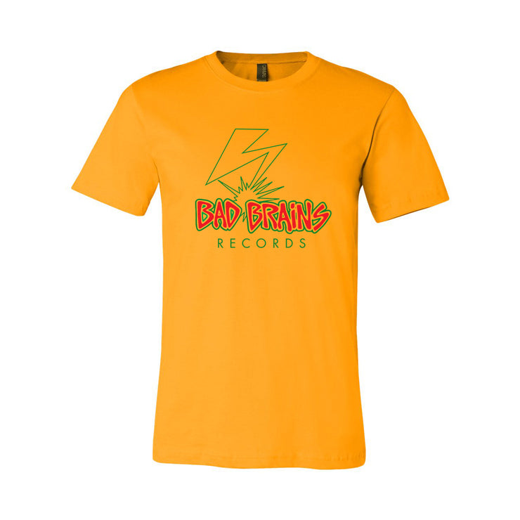 Photo of a gold tshirt against a white background. The shirt features the bad brains logo- it says Bad Brains in red lettering outlined in yellow and then outlined again in green. Below that in green reads "records". Above the text is a lightning bolt that is outlined in green, with no fill color.