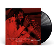Image of a vinyl sleeve and black vinyl against a white background. The vinyl sleeve is an Image of the bad brains- quickness punk note edition album cover. The artwork is a red photograph of the lead singer singing into a microphone. At the bottom of the image in white letters it says "Dr. Know, H.R., Earl Hudson, Darryl Jenifer. 1989 stereo punk note. In black text it says quickness. Next to that in white text it says bad brains.