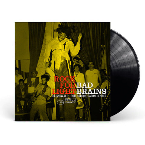 photo of a bad brains rock for light vinyl sleeve and black vinyl against a white background. The album cover is a yellow photograph that shows the band performing for a crowd. The singer is front and center, jumping in the air. The guitarist and fans can be seen in the background. At the bottom of the image in red letters it says rock for light. Next to that in white it says bad brains. Below this in white text it says "Dr. Know, H.R., Earl Hudson, Darryl Jenifer. "1983 stereo punk note".